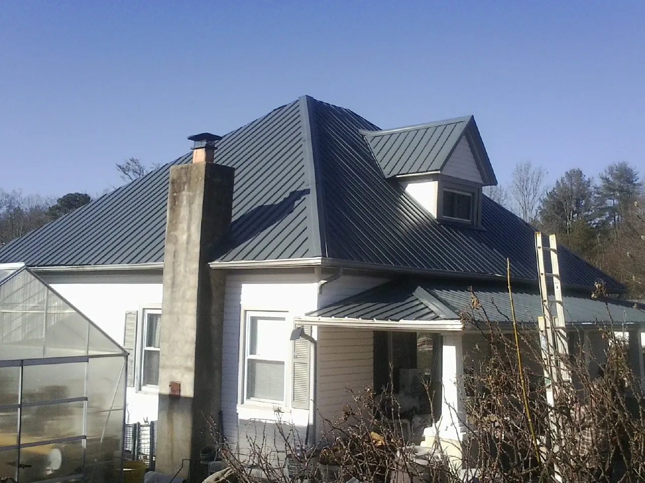 Dark blue standing seam metal roof on a white farmhouse with dormer — Slate & Tile Roof Repair by Roofing Brothers in Gilsum