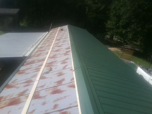 Old rusted panels beside newly installed green metal roofing — Wind Damage Roof Repair by Roofing Brothers in Gilsum