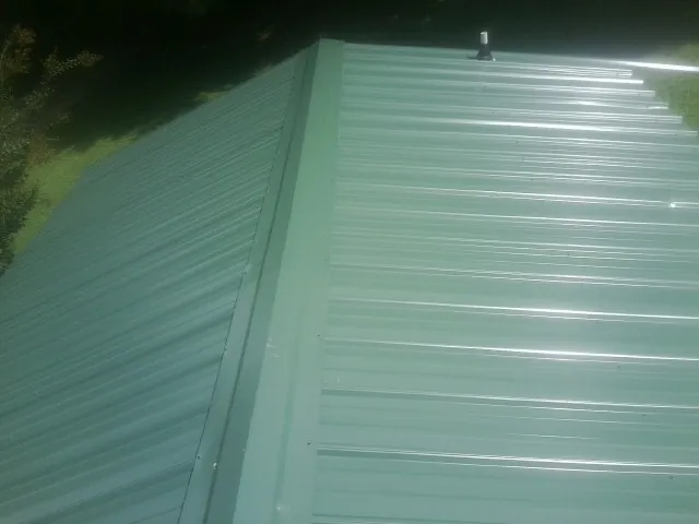New green metal panels meeting at the ridge of a roof — Flat Roof Repair work by our crew in Gilsum