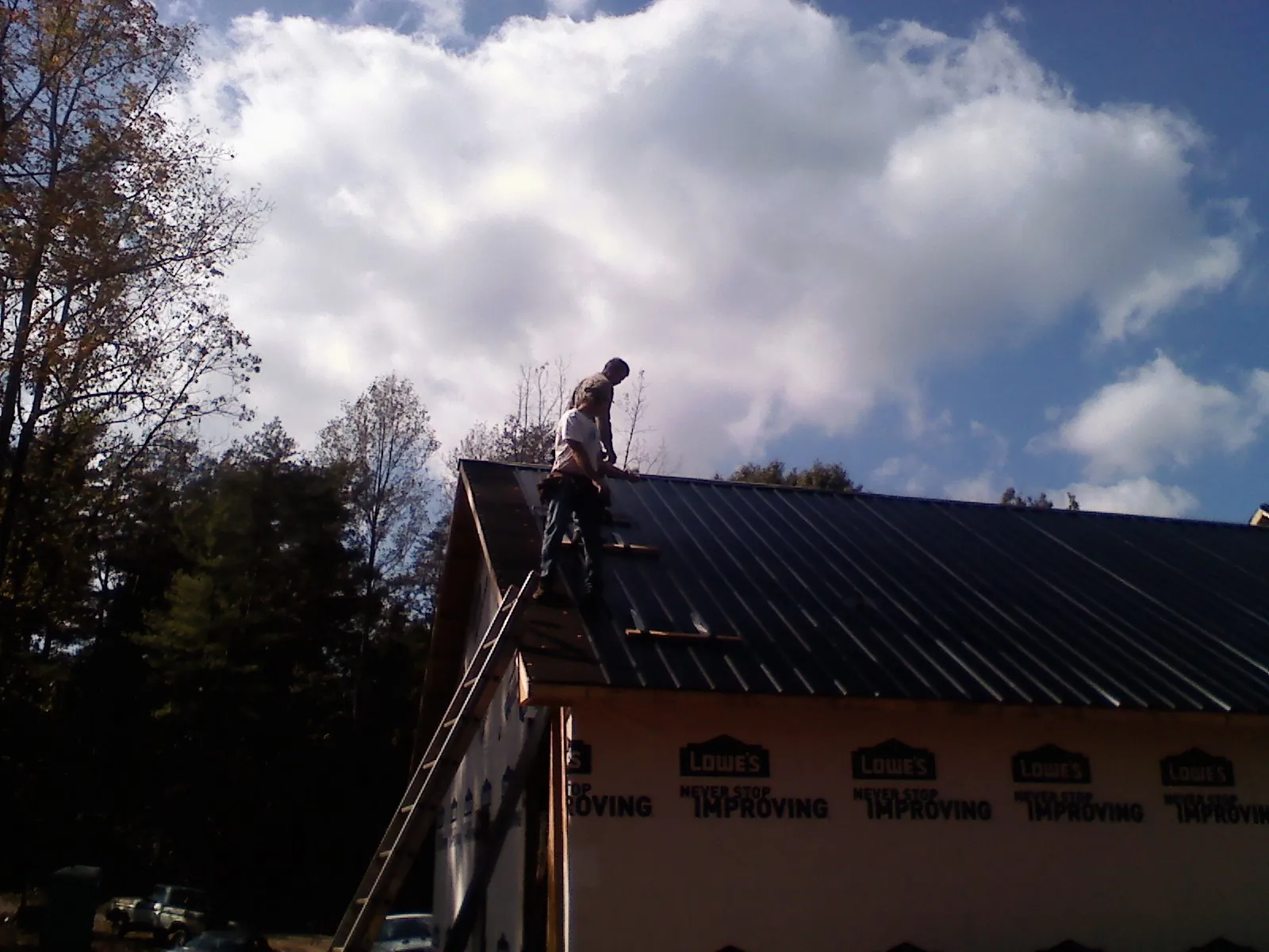 Roofer fastening dark metal panels high against a cloudy sky, from a Roof Inspection job in Gilsum