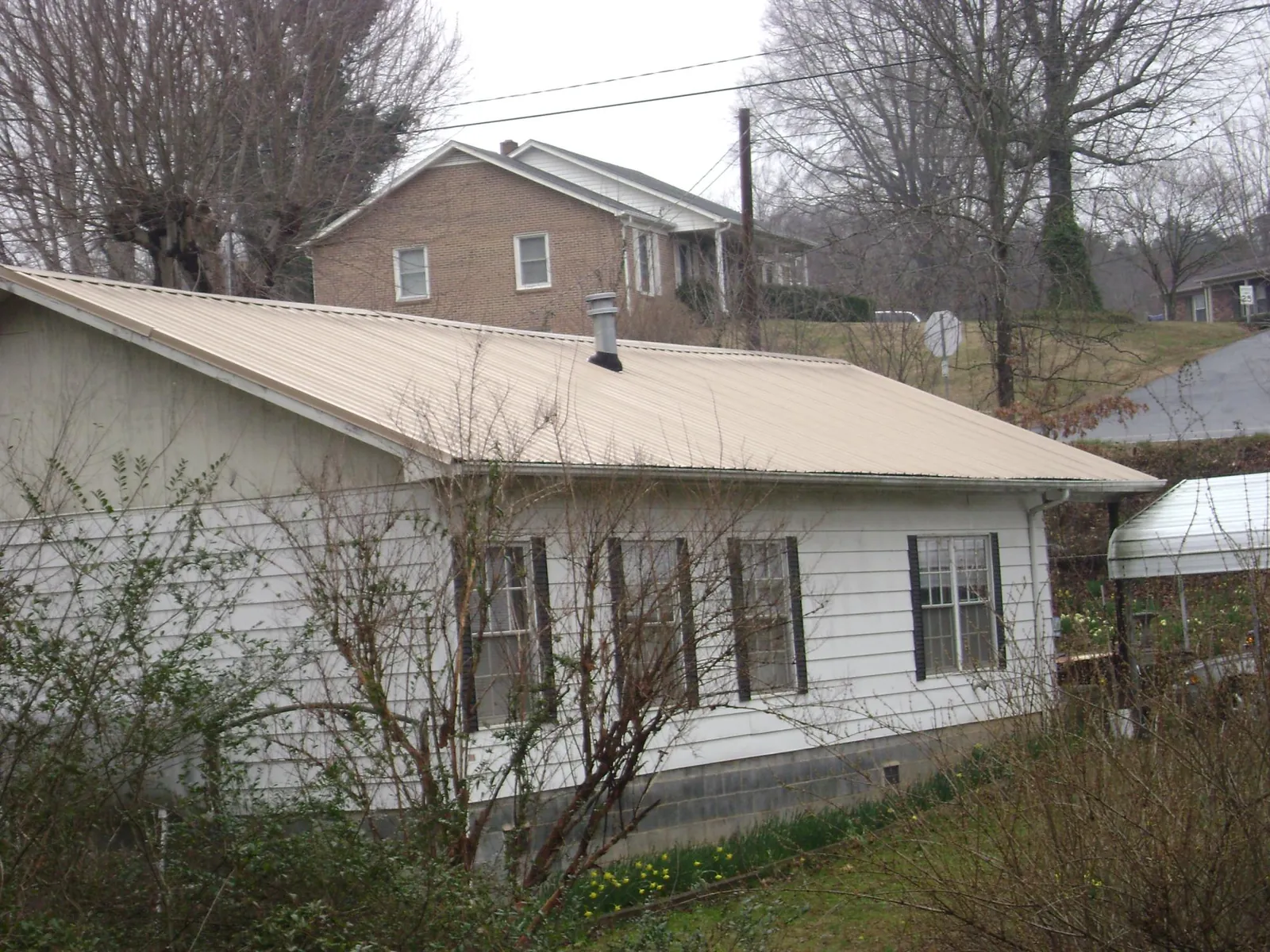 Tan metal roof on a white sided house set into a hillside — Commercial Roofing by Roofing Brothers in Gilsum